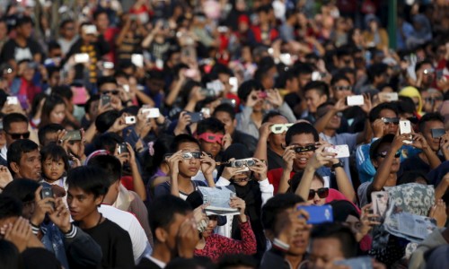 People watch a solar eclipse near the Ampera Bridge along the banks of the Musi River in Palembang, South Sumatra province, Indonesia March 9, 2016. REUTERS/Darren Whiteside