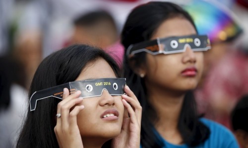 People watch a solar eclipse near the Ampera Bridge along the banks of the Musi River in Palembang, South Sumatra province, Indonesia March 9, 2016. REUTERS/Darren Whiteside