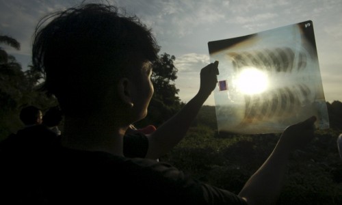 A person uses a medical X-ray film to view the sun during a solar eclipse in Silaut, West Sumatra province, Indonesia March 9, 2016 in this photo taken by Antara Foto. REUTERS/Iggoy el Fitra/Antara Foto