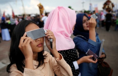 People test filters for watching a solar eclipse near the Ampera Bridge on the Musi River the day before thousands of people are expected to gather to witness the event in Palembang, South Sumatra province, Indonesia March 8, 2016. REUTERS/Darren Whiteside