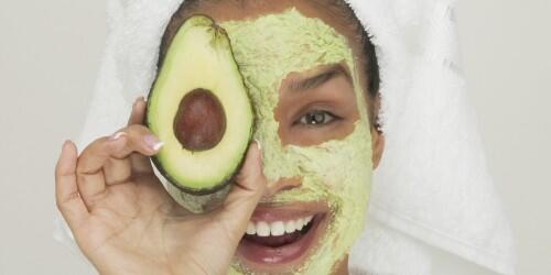 Portrait of a young woman wearing a facial mask holding a slice of avocado