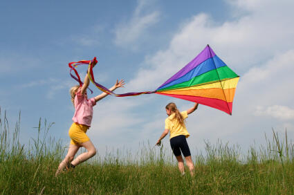 Children flying rainbow kite in the meadow on a blue sky background