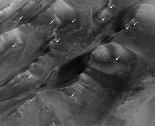 The white arrows indicate locations in this scene where numerous seasonal dark streaks, called "recurring slope lineae," have been identified in the Coprates Montes area of Mars' Valles Marineris by repeated observations from orbit. Credits: NASA/JPL-Caltech/Univ. of Arizona